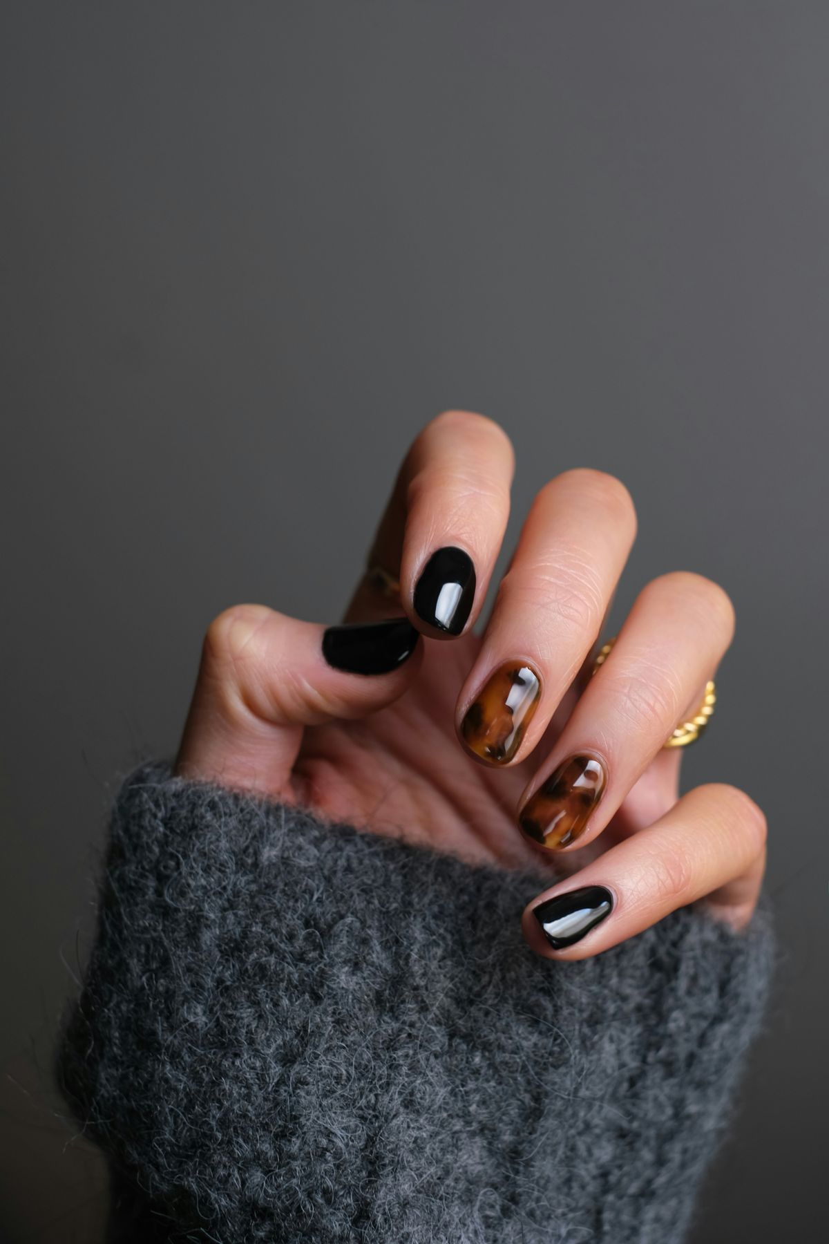 Hands with a dark manicure against a grey jumper