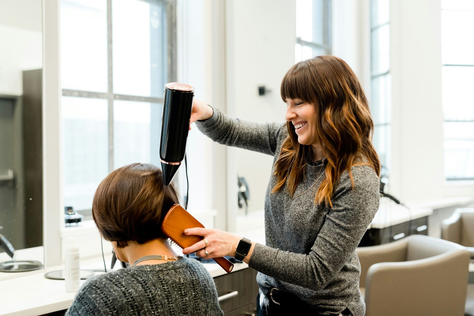 A stylist blow-drying a client's hair and laughing